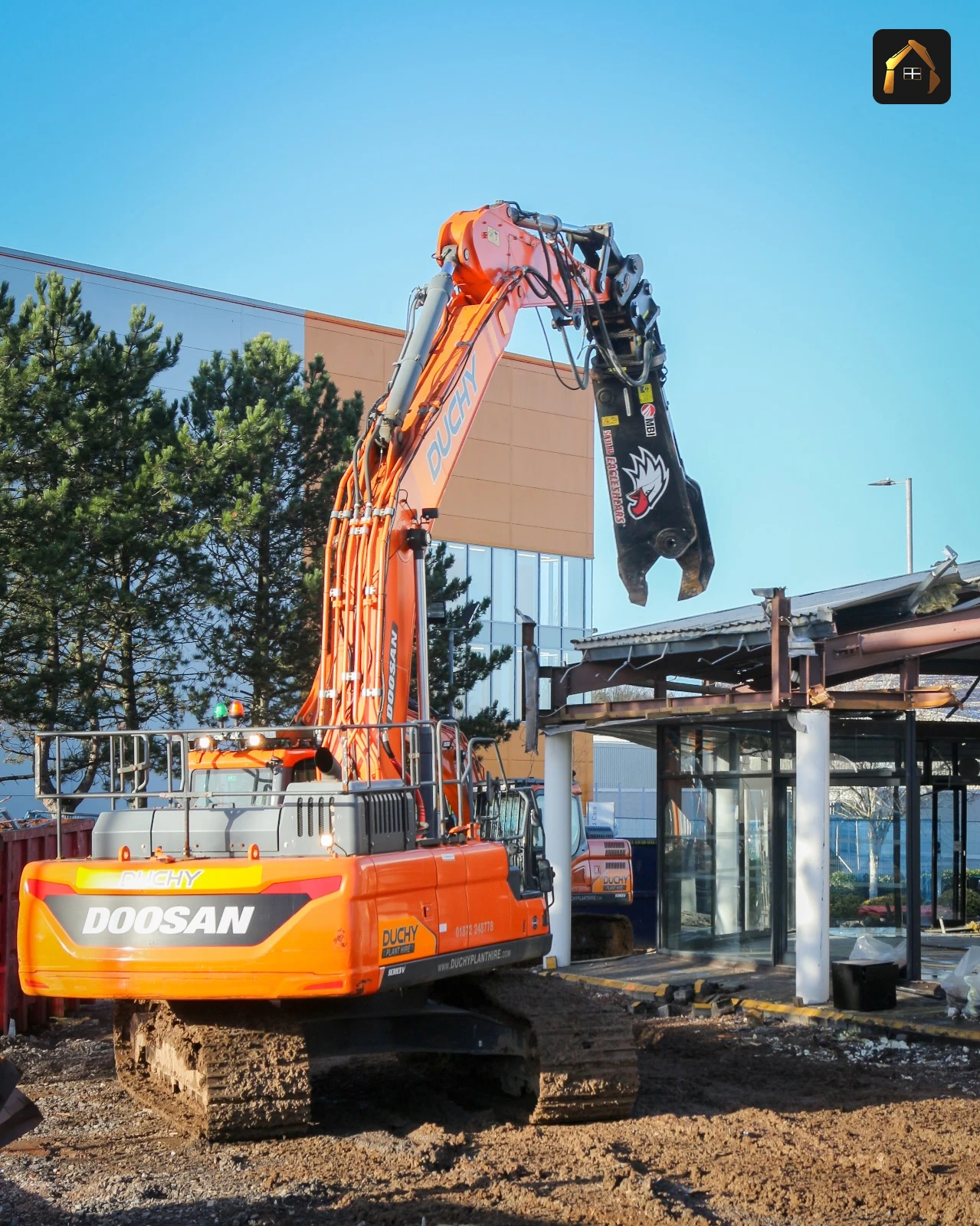Excavator on the cleared apron with the BMW showroom frame behind in Exeter