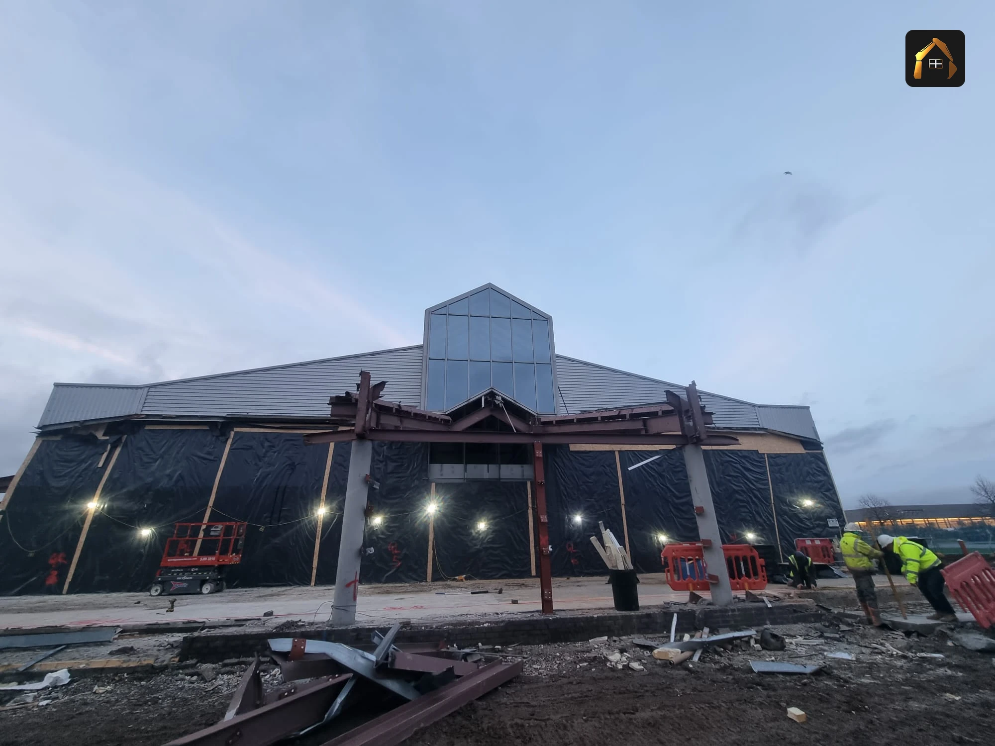 Exposed steel frame of the showroom lit up at dusk during demolition in Exeter