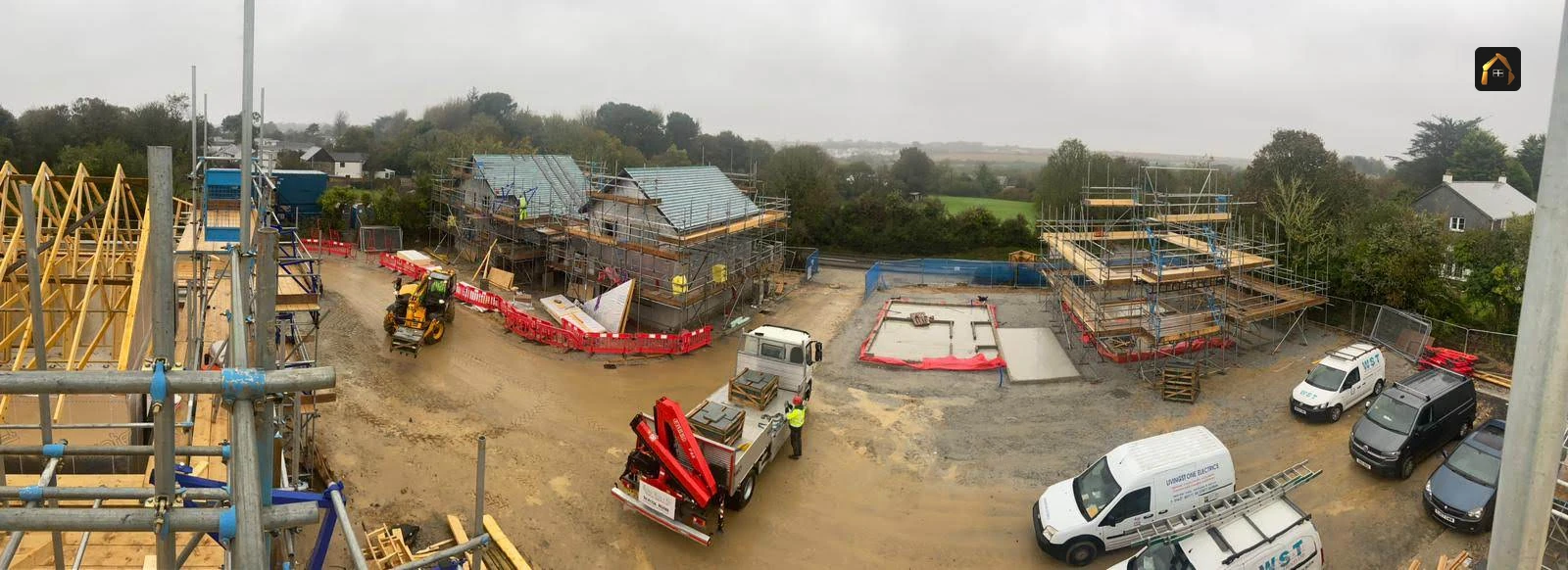 Wide view of a housing site with formwork, plant and houses under construction in Goonhavern
