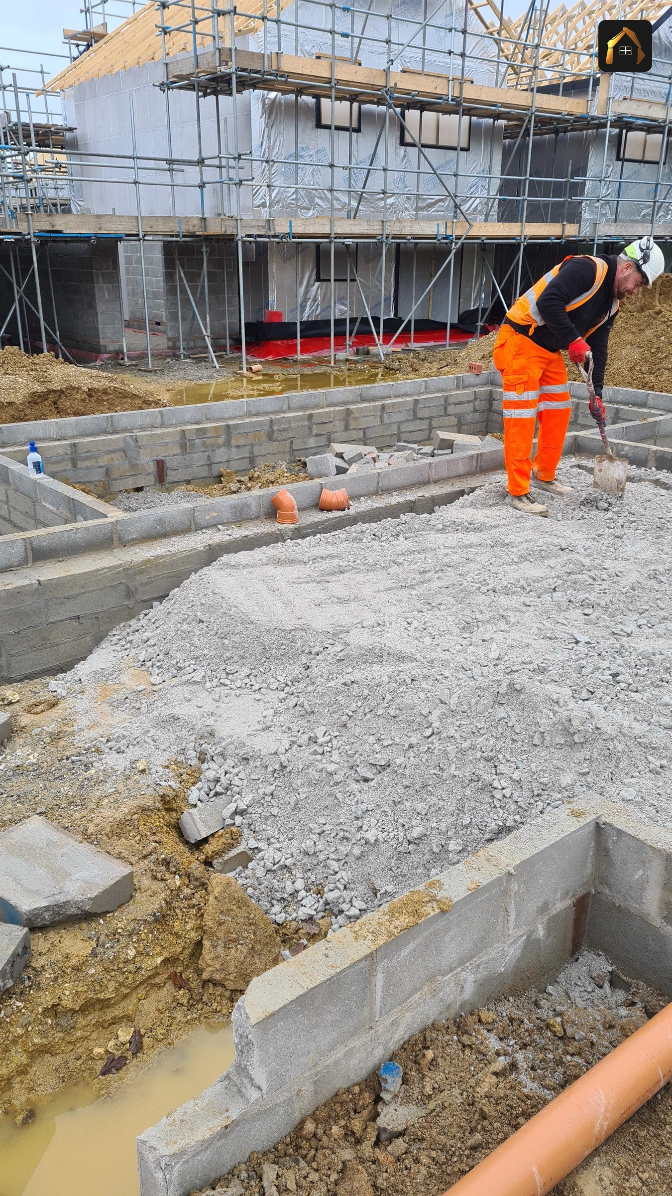 Worker in orange hi-vis at a scaffolded block on a housing site in Goonhavern