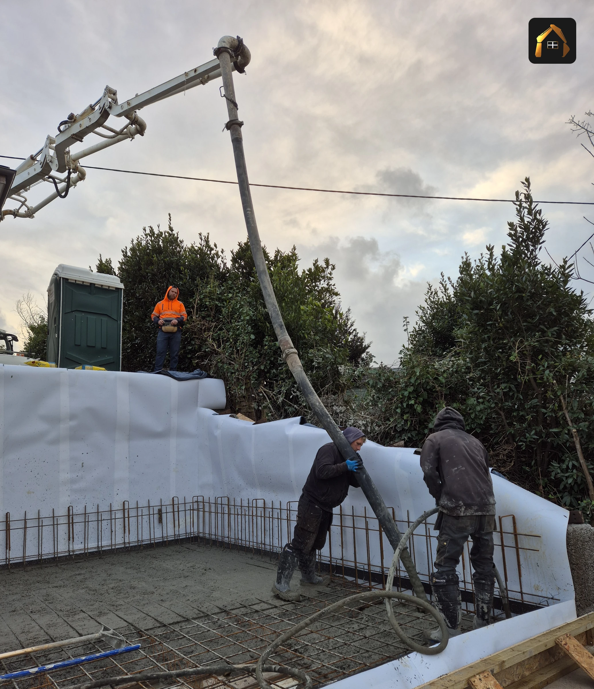 Two workers placing concrete from a pump hose into retaining wall formwork in Helford