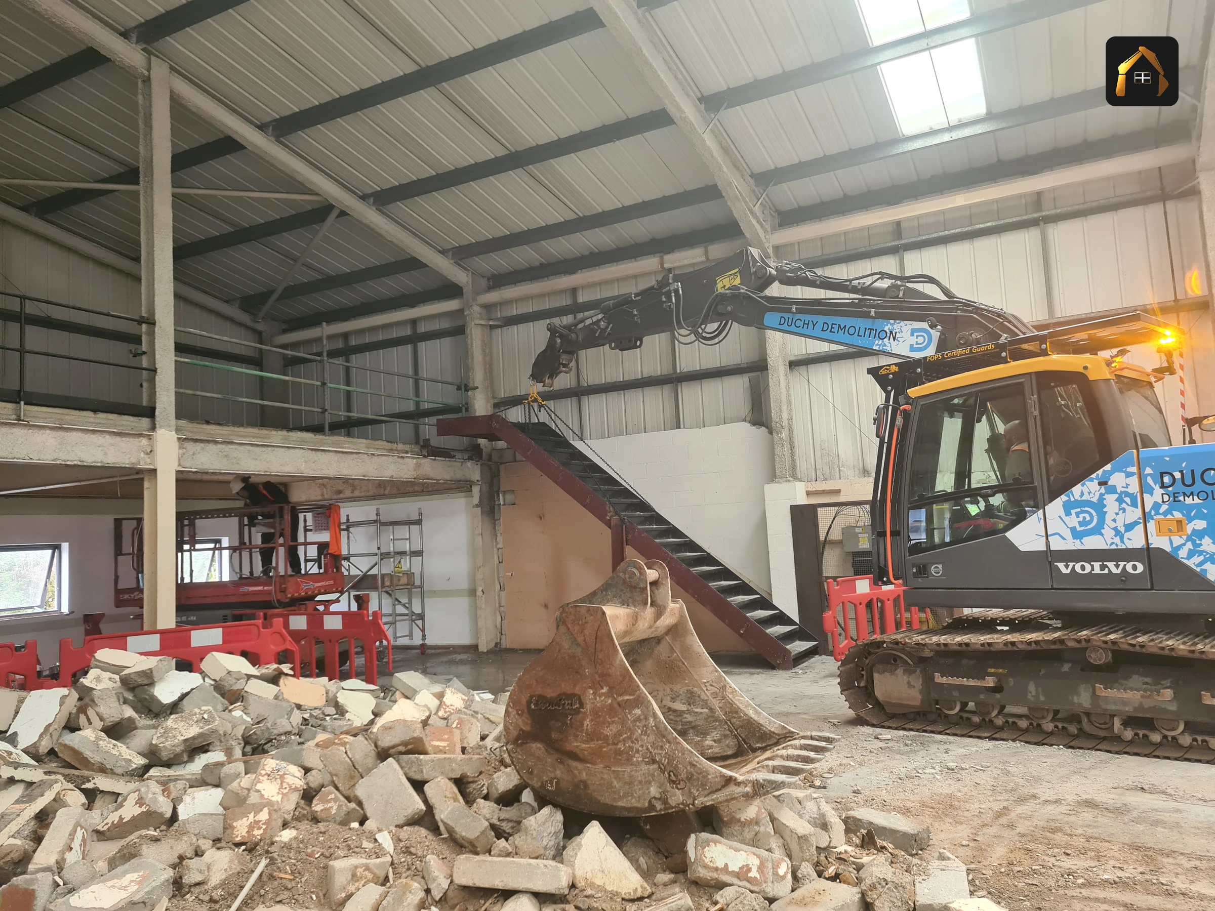 Excavator loading masonry rubble beneath the steel portal frame at Fal Fish in Redruth