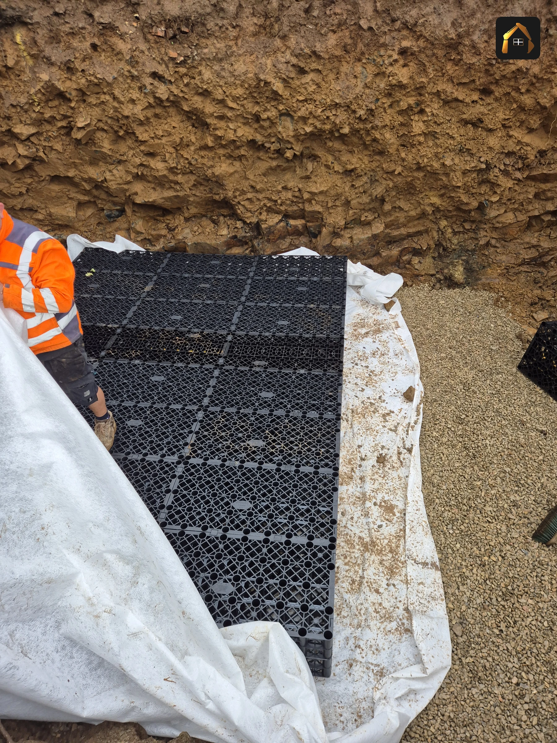 Groundworker placing attenuation crates onto geotextile in the soakaway excavation at Carrick Lodge, St Ives