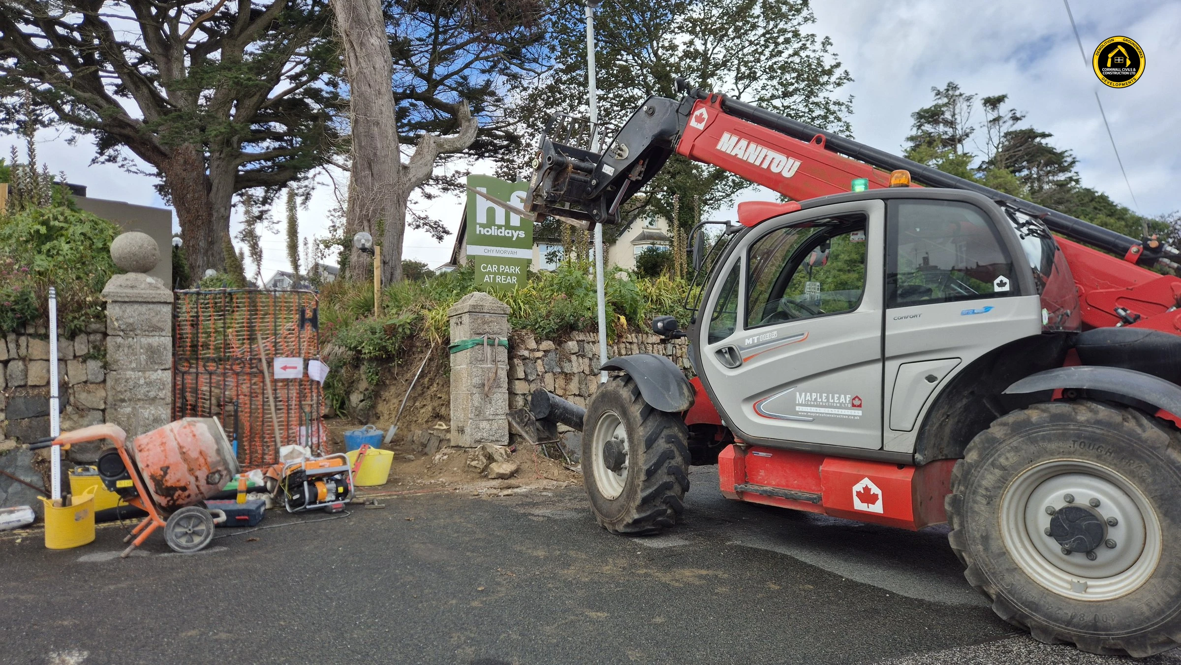 Telehandler beside a granite gate pier on the fenced Cornish hedge site in St Ives
